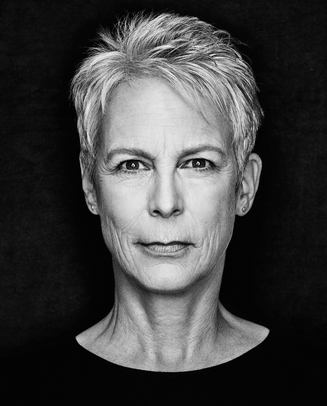 Black and white portrait of an adult female with short grey hair looking directly at the camera against a black background.
