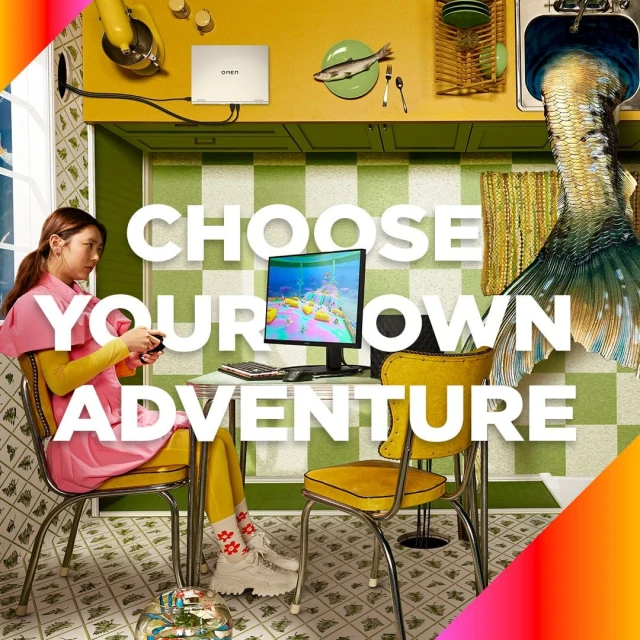 A young woman plays video games in a whimsical kitchen with a computer, fishbowl, and a mermaid tail coming from the sink.