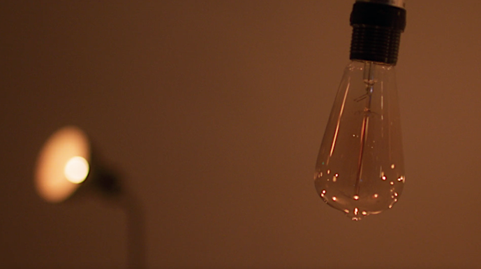 Close-up of a hanging Edison bulb against a blurred warm-toned background, casting a soft glow in an indoor setting.