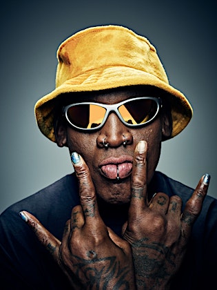 Portrait of an adult man wearing a yellow bucket hat and sunglasses, sticking his tongue out and holding up the 'rock on' hand gesture.