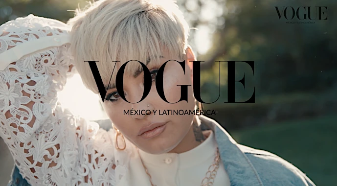 Woman with blonde pixie cut poses for Vogue Mexico & Latin America, wearing a lace top and gold jewelry, against a green background.