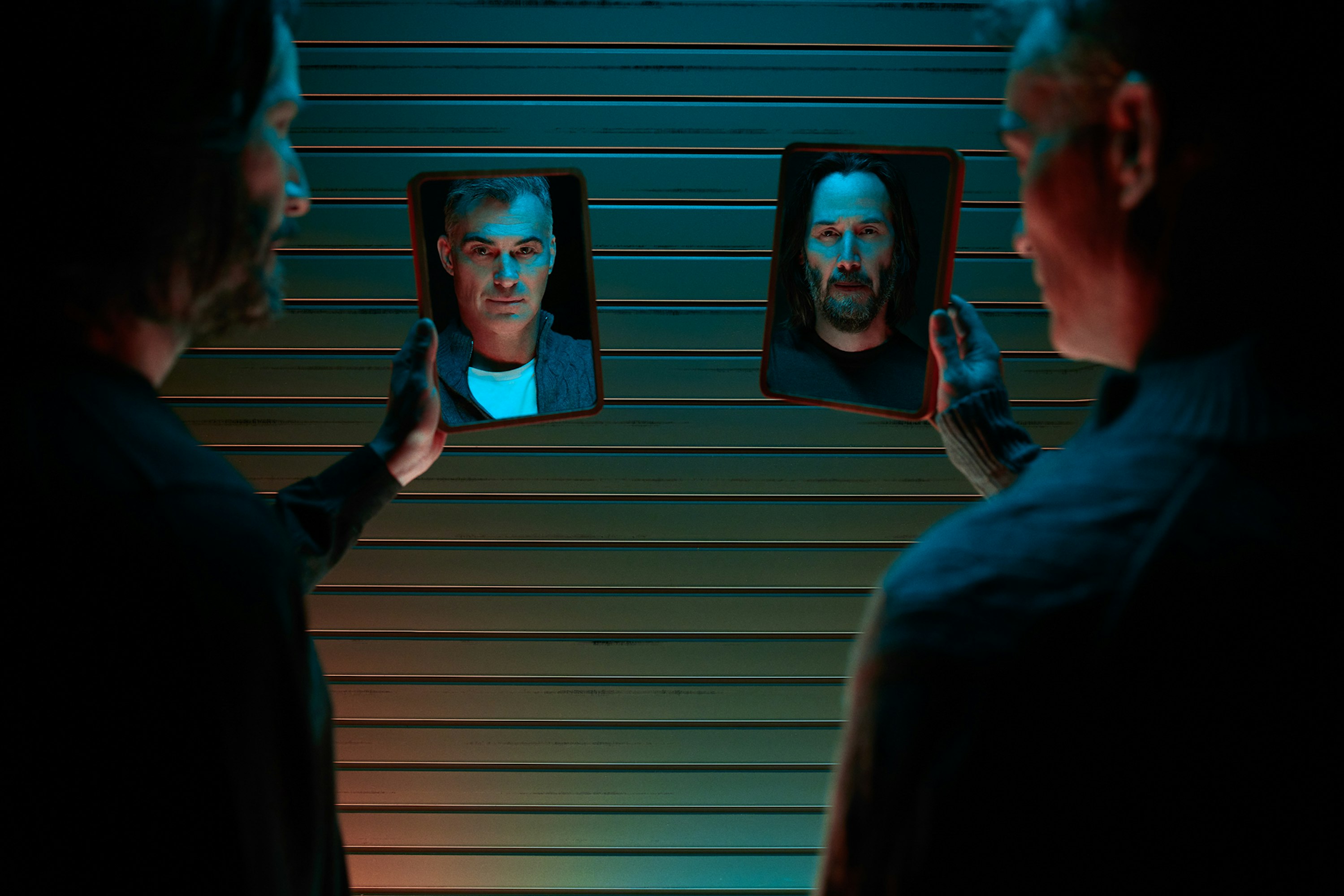 Two people hold up tablets displaying portraits, facing each other against a blue horizontally-striped wall in an indoor setting.