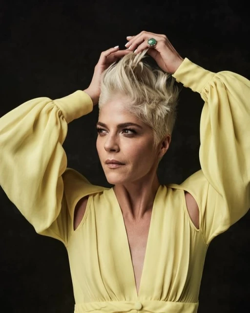 Close-up portrait of a blonde adult woman with short hair in a yellow dress, looking off to the side against a dark background.