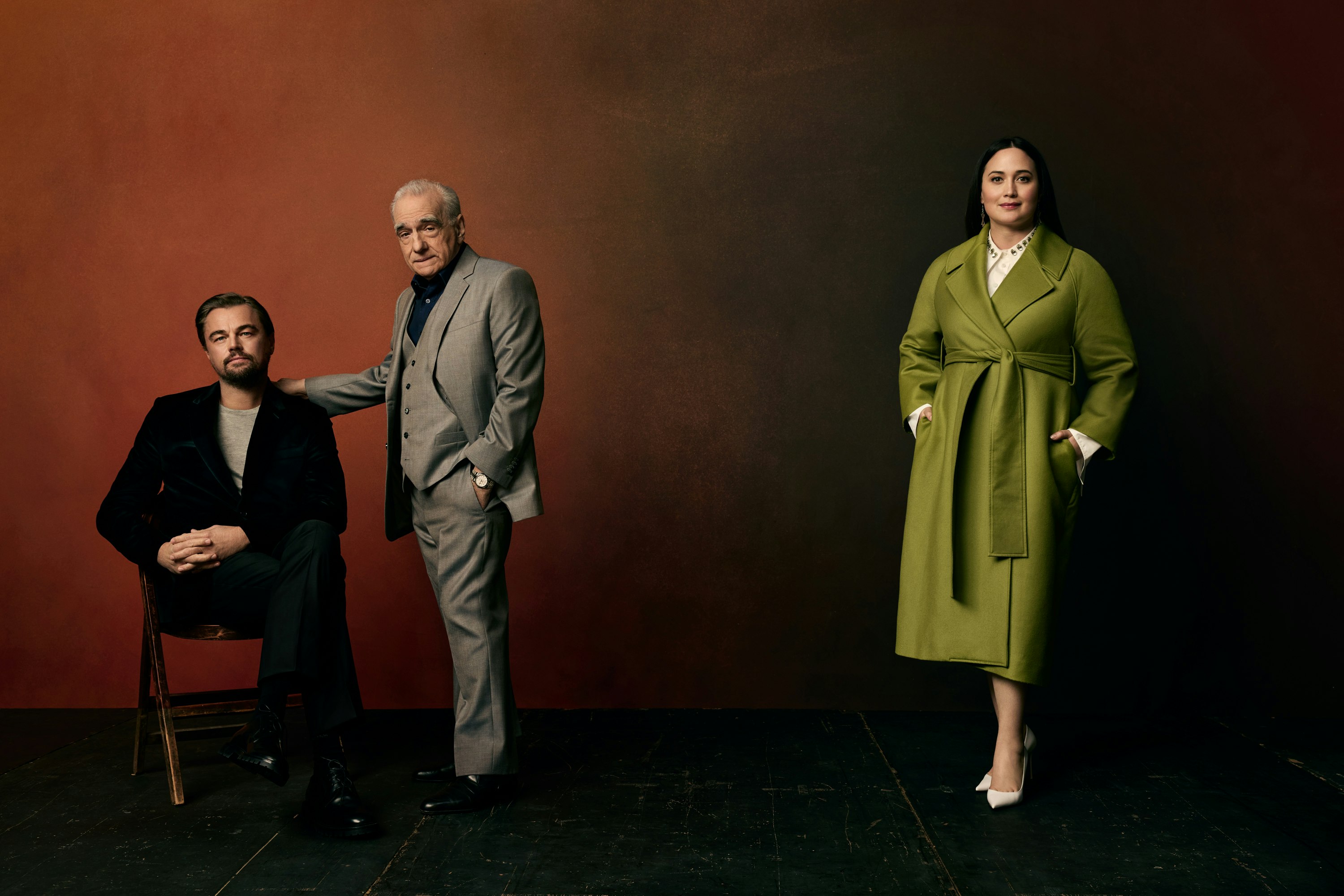 Three people, Leonardo DiCaprio, Martin Scorsese, and Lily Gladstone, pose in front of a mottled backdrop in a studio shot.
