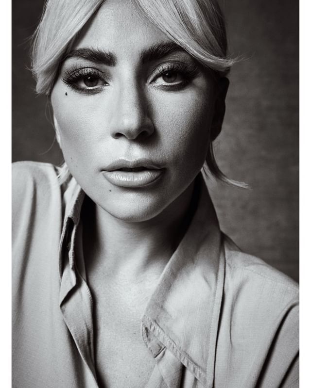 Close-up monochrome portrait of Lady Gaga wearing a buttoned collared shirt against a textured background