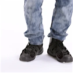 Lower portion of a person wearing blue jeans and black shoes standing against a white background in a brightly lit indoor setting.