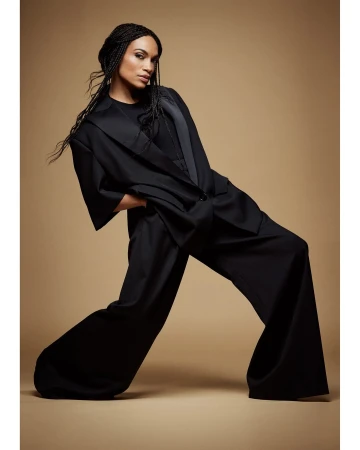 Model with long braided hair wearing an oversized black suit posing against a warm neutral background