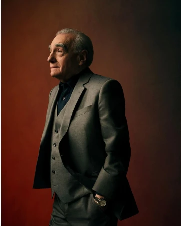 Portrait of Martin Scorsese in a grey three-piece suit against a dark reddish-brown studio backdrop by Art Streiber.