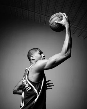 Monochrome portrait of a basketball player holding a basketball overhead against a plain background.