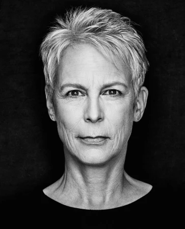 Close-up portrait of Jamie Lee Curtis with short grey hair and a serious expression against a dark textured background