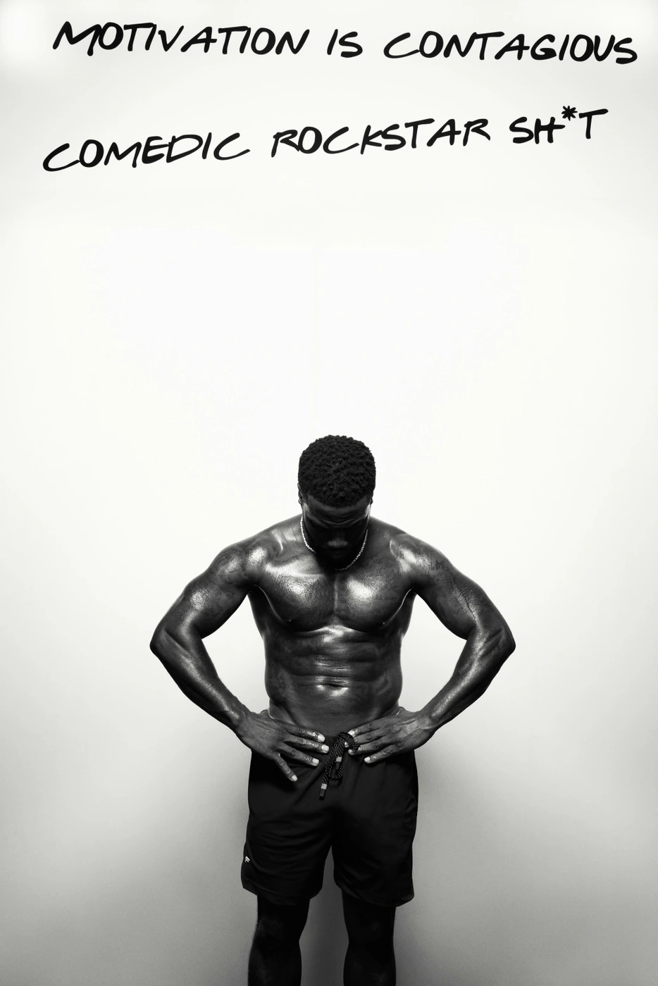 Black and white portrait of a muscular man standing shirtless with hands on waist against a plain white studio wall.