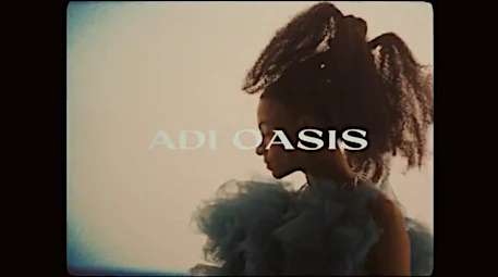 A woman with dark hair stands in profile wearing a blue tulle dress against a cream background with text overlay in a studio environment.