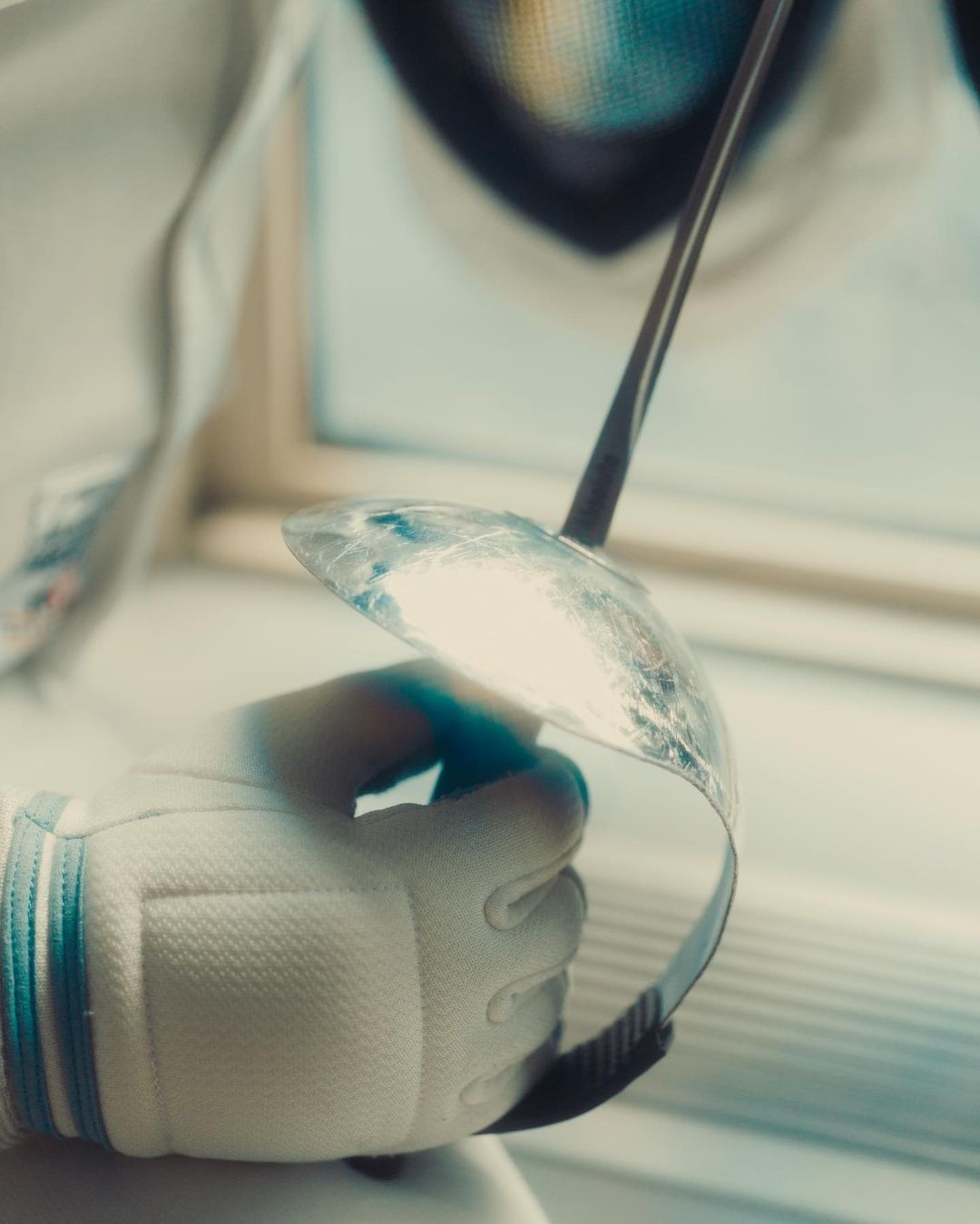 Close-up of a gloved hand holding a fencing foil indoors, highlighting the sport's precision and focus on technique with neutral tones.