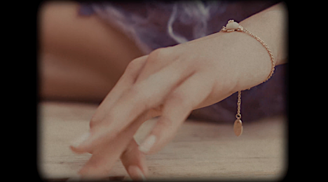 Close-up of a woman's hand with manicured nails wearing a gold bracelet on a wooden surface, captured with a vintage lens effect.