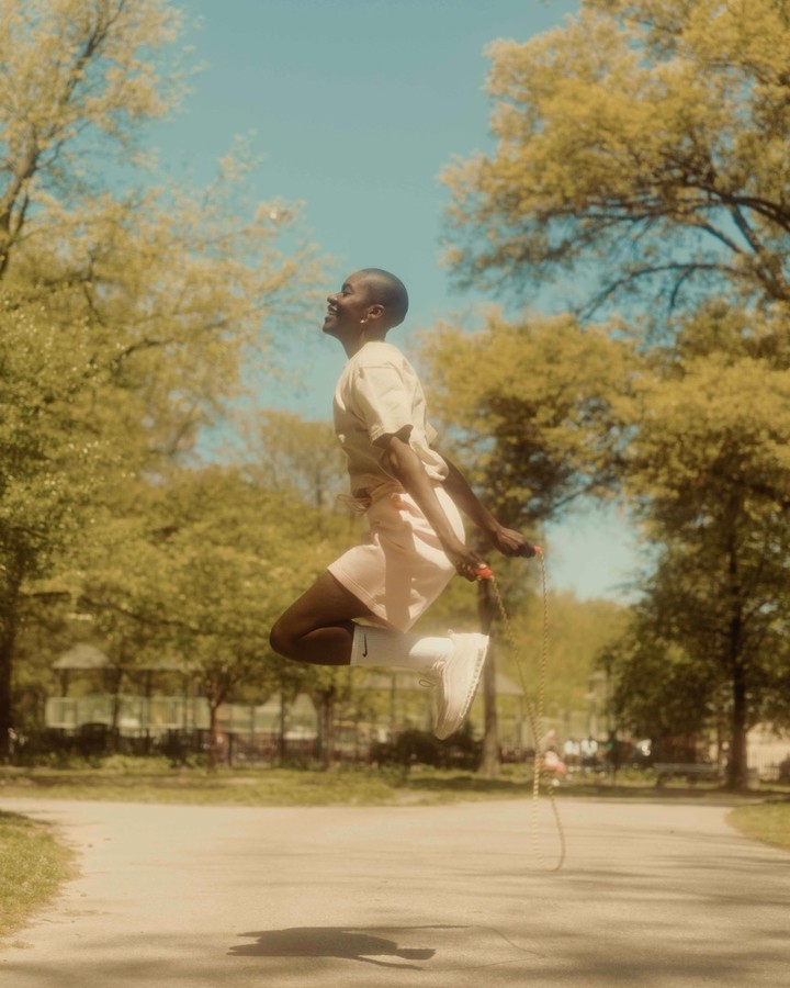 Adult woman leaping mid-air with a jump rope in a sunny park setting, wearing sportswear, capturing a dynamic moment of fitness.