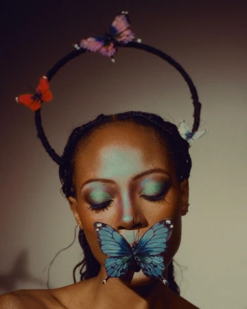 Close-up portrait of a Black woman with closed eyes wearing a blue butterfly over her lips and a circular halo headpiece with decorative butterflies