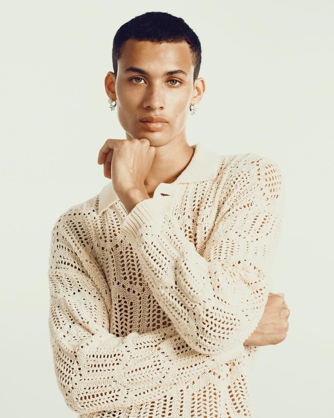 Portrait of a light-skinned adult male with short dark hair, wearing a white knitted sweater against a white background in a studio.