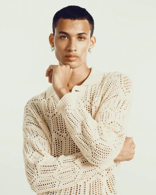 Portrait of a light-skinned adult male with short dark hair, wearing a white knitted sweater against a white background in a studio.