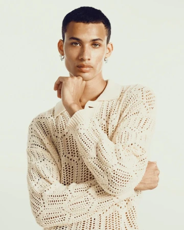 Portrait of a light-skinned adult male with short dark hair, wearing a white knitted sweater against a white background in a studio.