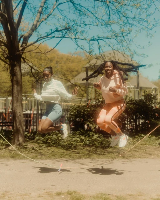 Two women in activewear jump rope outside on a sunny day, showcasing fitness and leisure in a vibrant park setting.