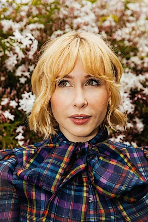 Portrait of a blonde woman wearing a plaid blouse with a bow collar against a floral background by Brinson+banks