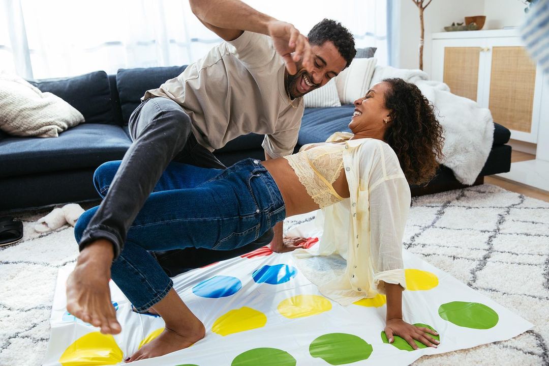 Playful couple shares a lighthearted moment indoors, joyfully engaging in a game of Twister, enhancing their connection and laughter.