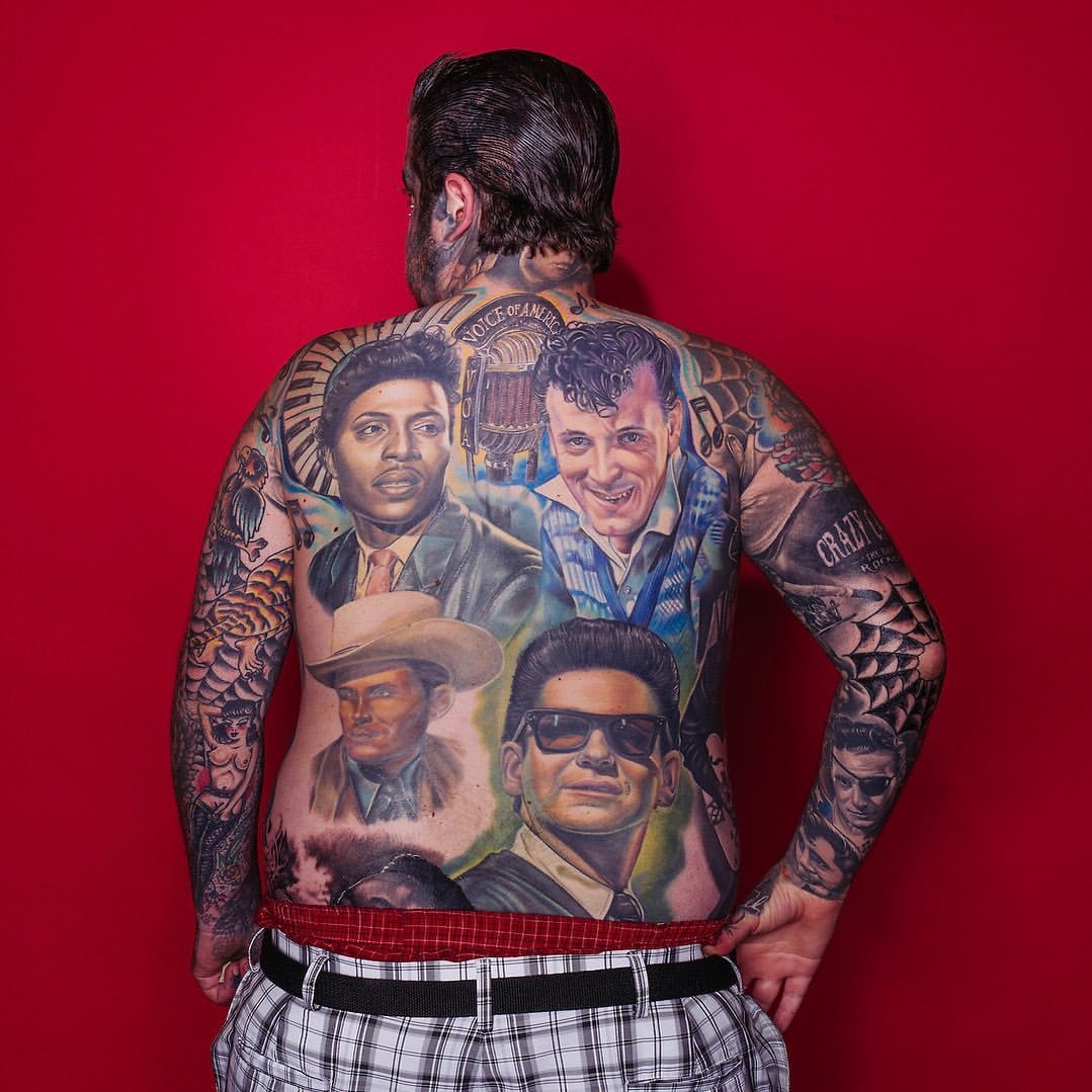 Man with back tattoos featuring portraits of musicians against a red backdrop. Detailed tattoo art on skin. Focus on tattoo detail.