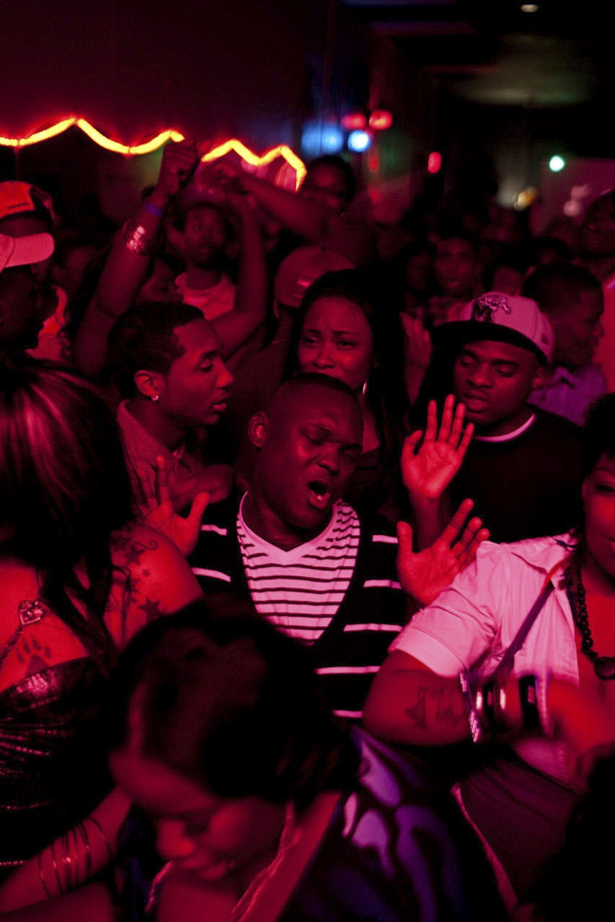 Nightclub scene featuring a crowd of adults dancing under red lighting and neon lights, creating a vibrant and energetic atmosphere.
