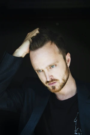 Close-up portrait of man with beard running hand through hair wearing dark blazer against dark background