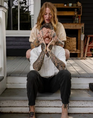 A woman covering a smiling man's eyes with her hands on a porch, photographed by Brinson+banks.