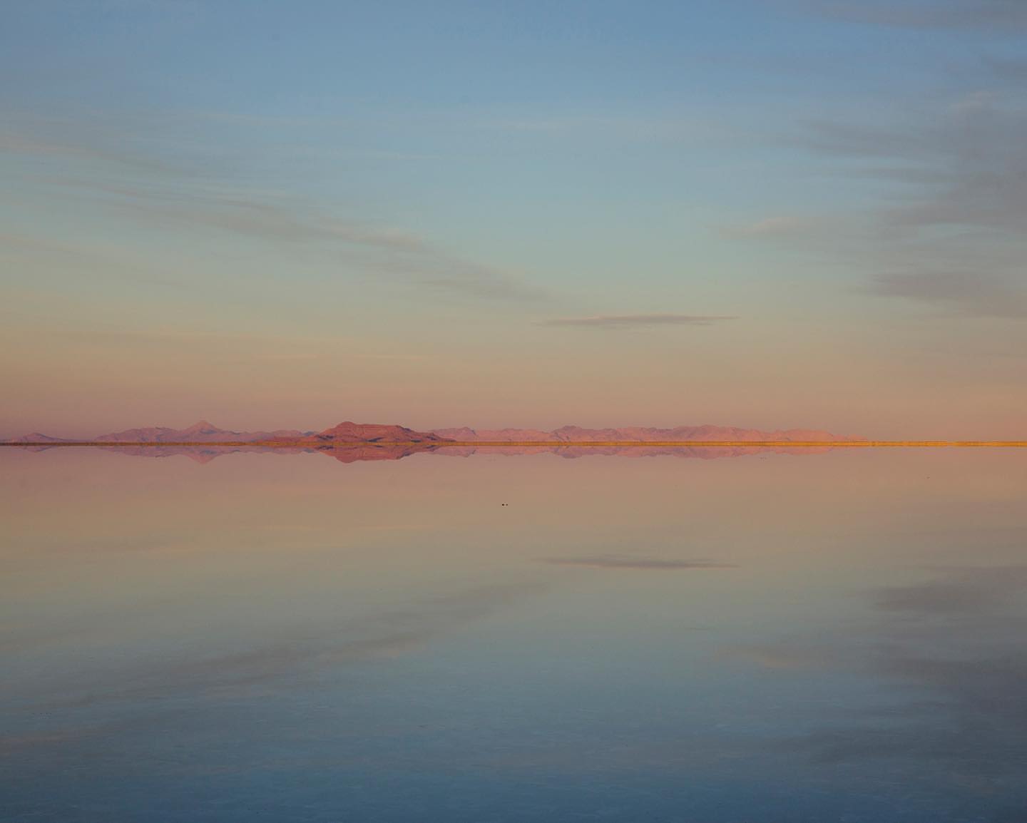 Abstract landscape featuring a serene lake reflecting a soft, colorful sunset sky with distant mountains, creating a peaceful vista.