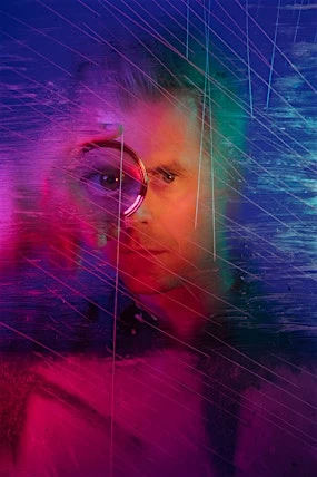 Surreal portrait of a male with light hair and round glasses; neon blue, green, and pink lighting effects overlay the image, creating a unique aesthetic.