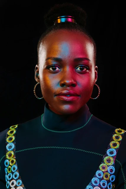 Close-up portrait of a woman with a high bun hairstyle, wearing decorative round earrings and a dark top with circle embellishments.