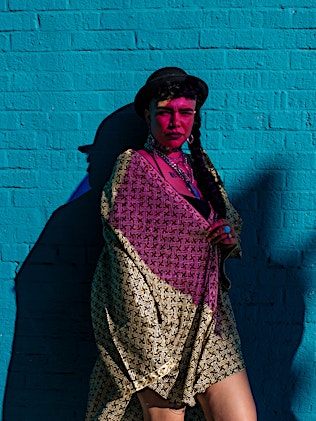 Woman in patterned kimono poses against a bright turquoise brick wall with a shadow cast on the side of her face and the wall.