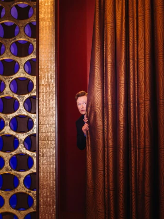 Man peeking from behind a heavy patterned curtain next to a decorative panel with circular cutouts