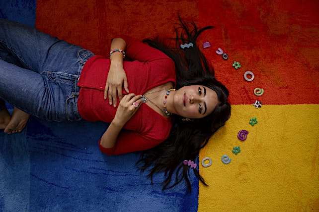 Young woman lying on colorful rug surrounded by playful hair accessories, showcasing a casual and cheerful fashion and lifestyle aesthetic.