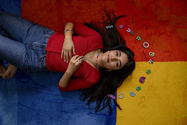 Young woman lying on colorful rug surrounded by playful hair accessories, showcasing a casual and cheerful fashion and lifestyle aesthetic.