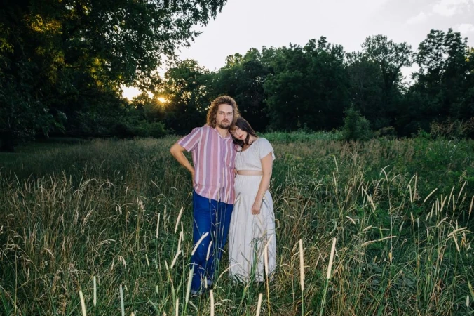 Man and woman standing together in a tall grass meadow at sunset, photographed by Brinson+Banks.