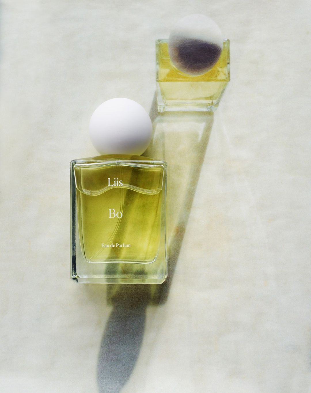 Close-up of two glass perfume bottles with spherical white caps on a white surface, highlighting the product's minimalist design.