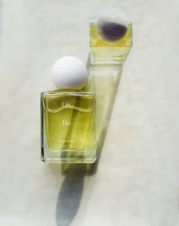 Close-up of two glass perfume bottles with spherical white caps on a white surface, highlighting the product's minimalist design.
