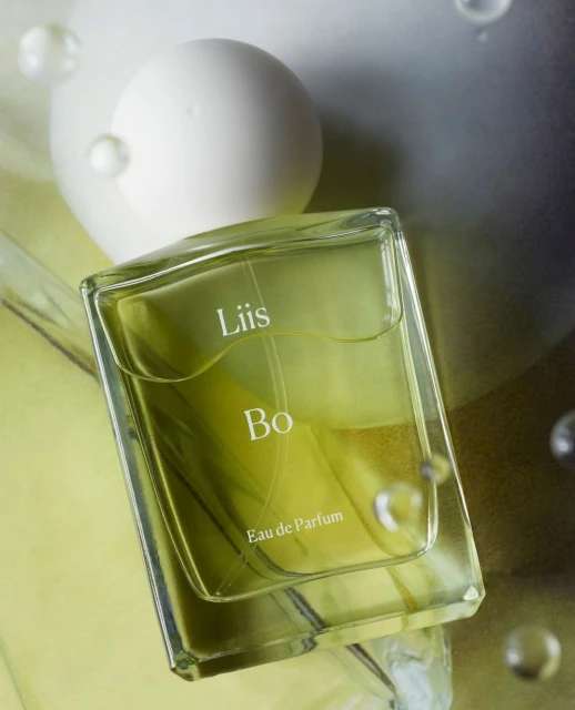 Close-up studio shot of a clear glass perfume bottle with the text 'Liis Bo Eau de Parfum' on a light green and white background.
