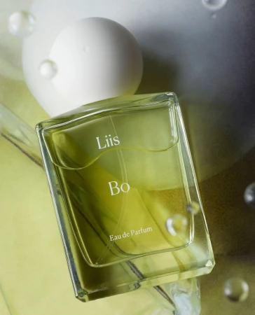 Close-up studio shot of a clear glass perfume bottle with the text 'Liis Bo Eau de Parfum' on a light green and white background.
