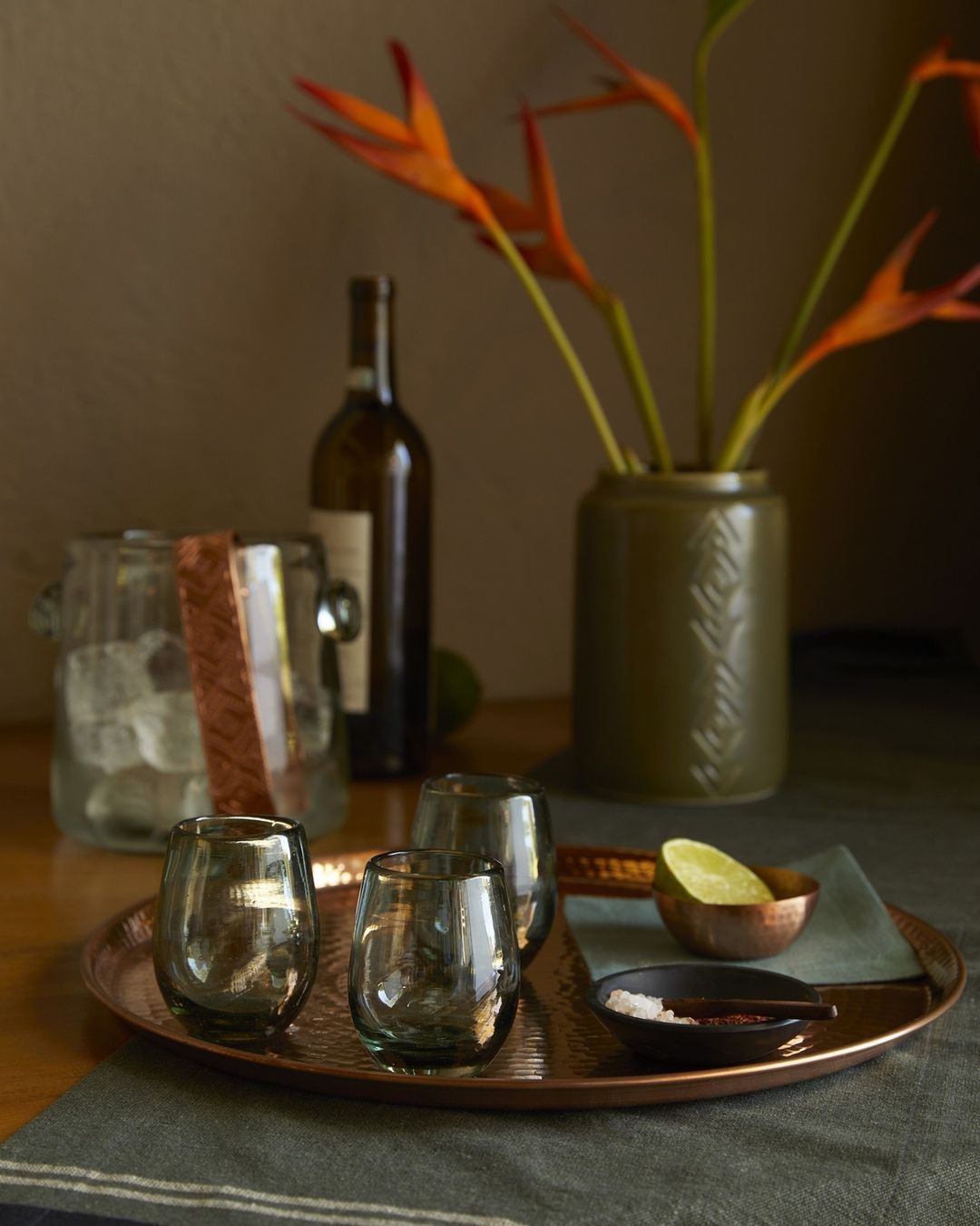 Still life shot with stemless glasses, ice bucket, wine bottle, copper tray, and citrus fruits, creating an elegant, muted mood.