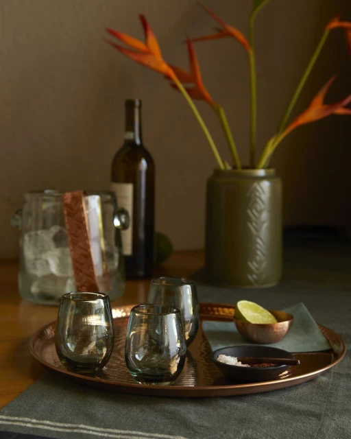 Still life shot with stemless glasses, ice bucket, wine bottle, copper tray, and citrus fruits, creating an elegant, muted mood.