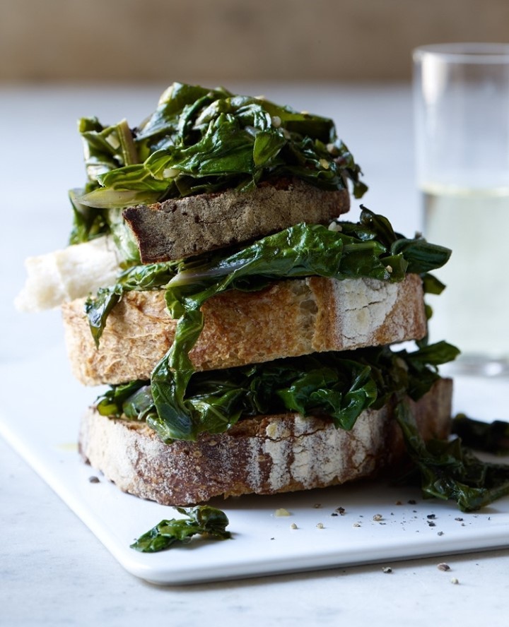 Stack of bread slices filled with green leafy vegetables and a glass of water. Food still life shot, emphasizing natural ingredients.
