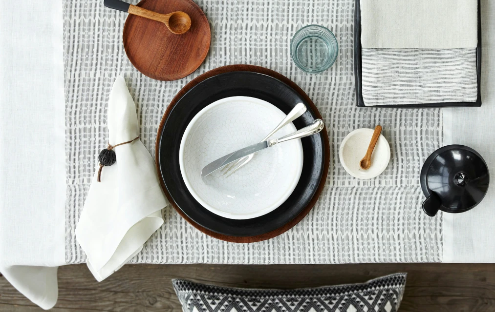 Overhead shot of a table setting with plates, silverware, napkins, and decorative elements on a patterned tablecloth.