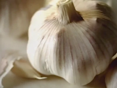 Close-up of a bulb of garlic with a creamy white hue. The image showcases the texture and details of the garlic bulb's outer layers.