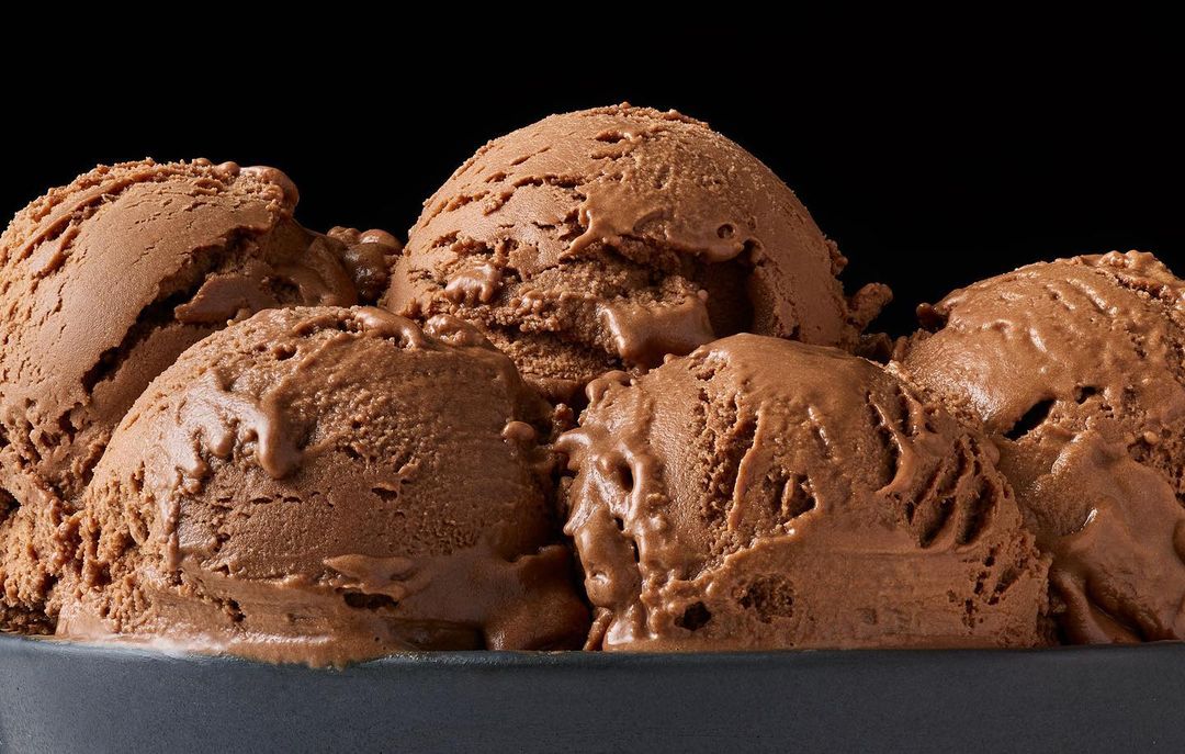 Close-up of several scoops of rich chocolate ice cream served in a dark grey bowl against a black background, food photography.