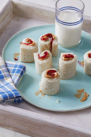 Peanut butter and jelly pinwheel sandwiches arranged on a blue plate with a glass of milk on a wooden tray for kids.
