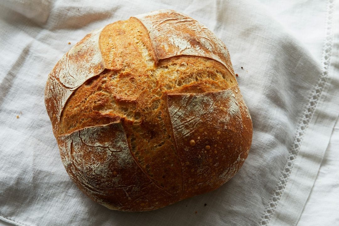 Overhead shot of a golden-brown loaf of crusty bread sitting on a textured white linen cloth, showcasing its rustic and appetizing appearance.